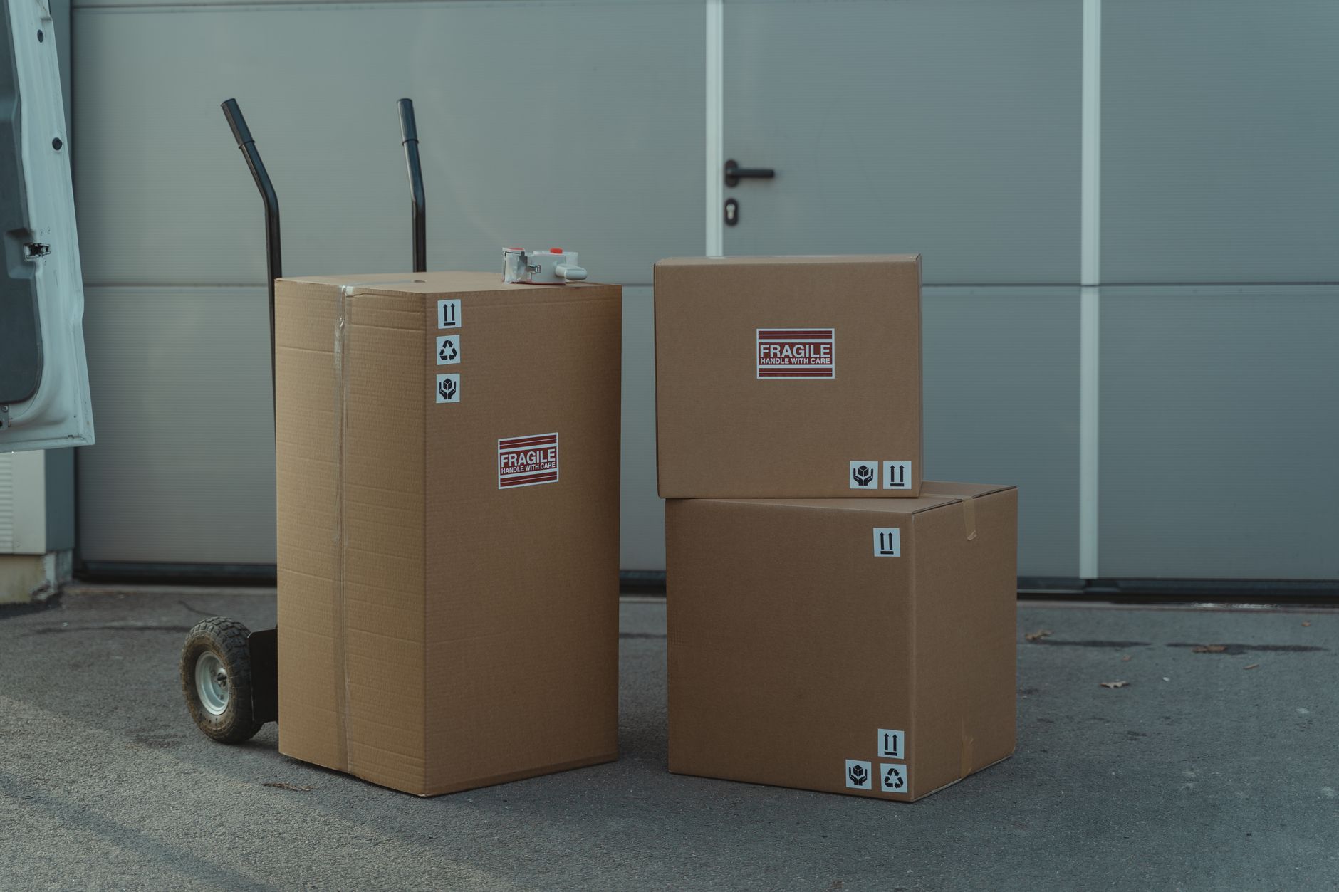 Stacked cardboard shipping boxes beside a hand truck at a loading bay